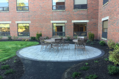 The custom patio, with paver slabs installed in a random pattern with contrasting dark border, is installed in a shady corner near the building.
