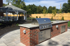The outdoor kitchen is fully equipped with a gas range, prep sink, trash receptacles, and a natural granite slab counter top.